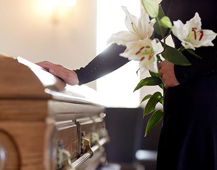 Woman with white lily flowers and coffin at funeral in church