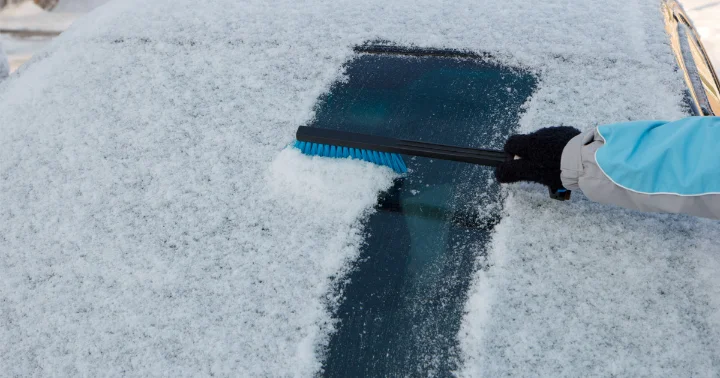 A person cleaning a car's windshield with a brush, removing dirt and debris for better visibility.